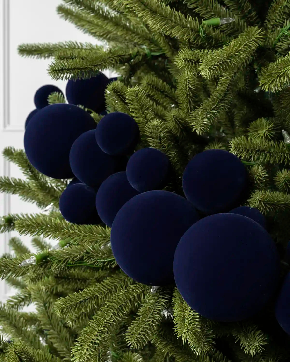 Dark navy blue velvet round ornaments hanging on a green artificial Christmas tree.