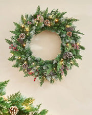 Decorated Christmas frosted wreath with pinecones, berries and lights on a cream wall 