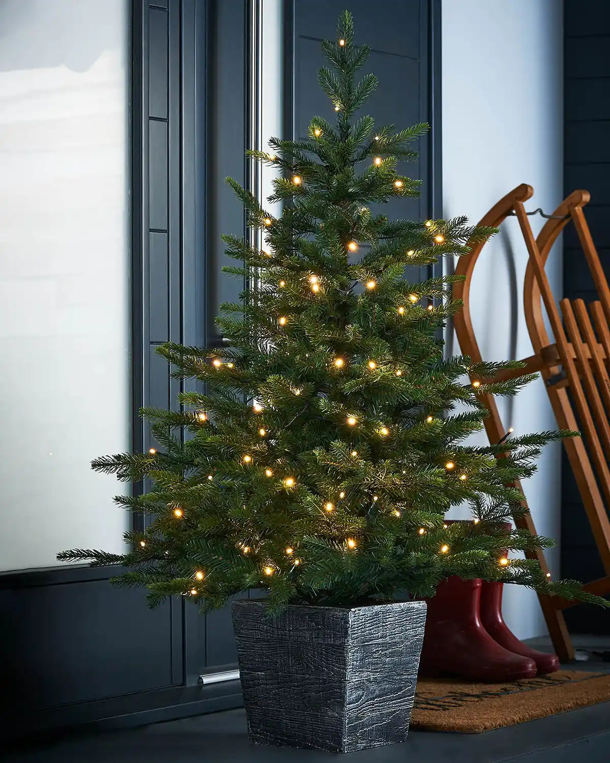 Decorated Pre-Lit Grand Fir Potted Christmas Tree, 4 ft with lights in a textured black pot on a doorstep 