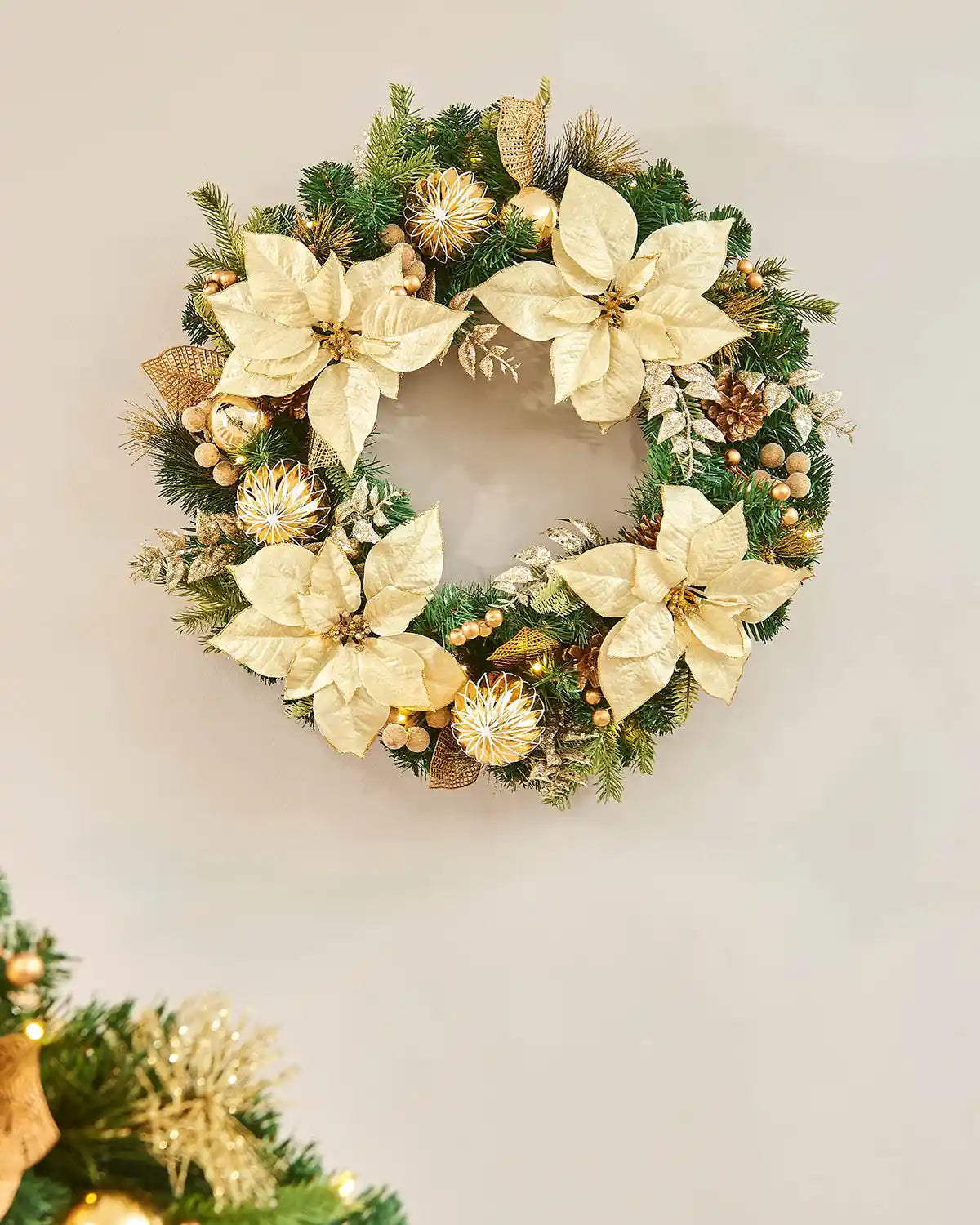 Decorated Wreath with cream flowers, gold baubles, pinecones and glitter leaves on a cream background