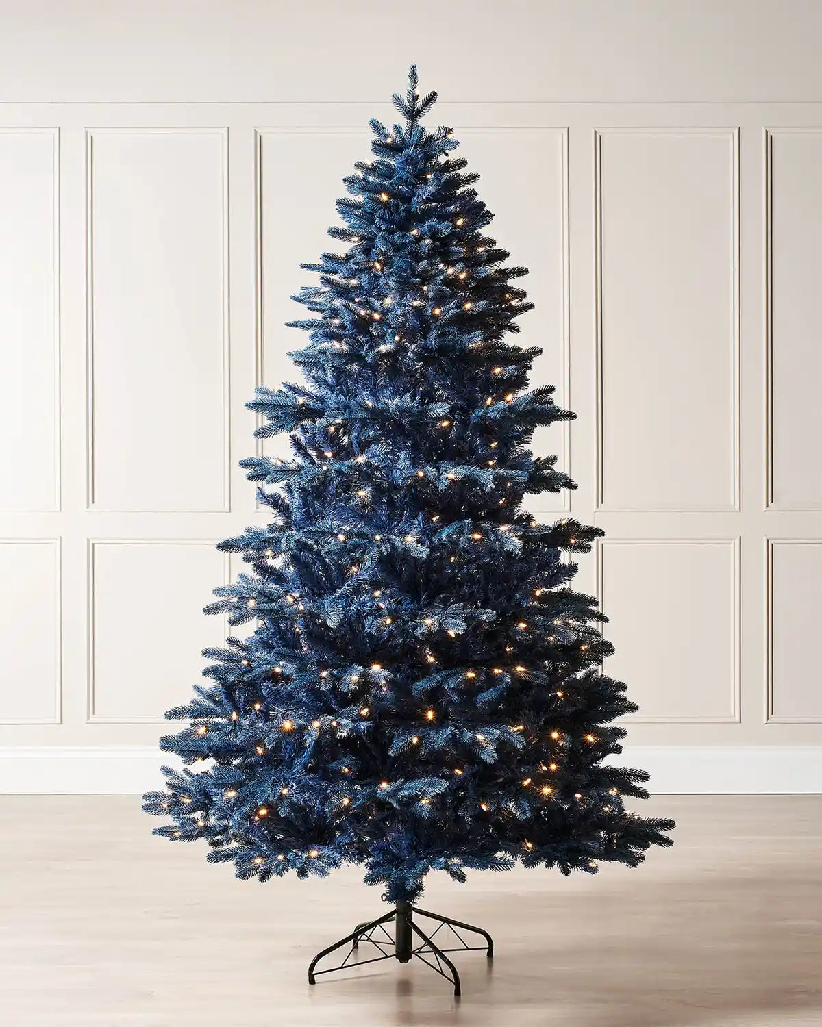 Decorated blue Christmas tree with lights against a cream panel wall.