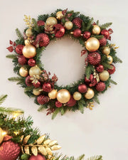 Decorated gold and burgundy wreath on a grey wall