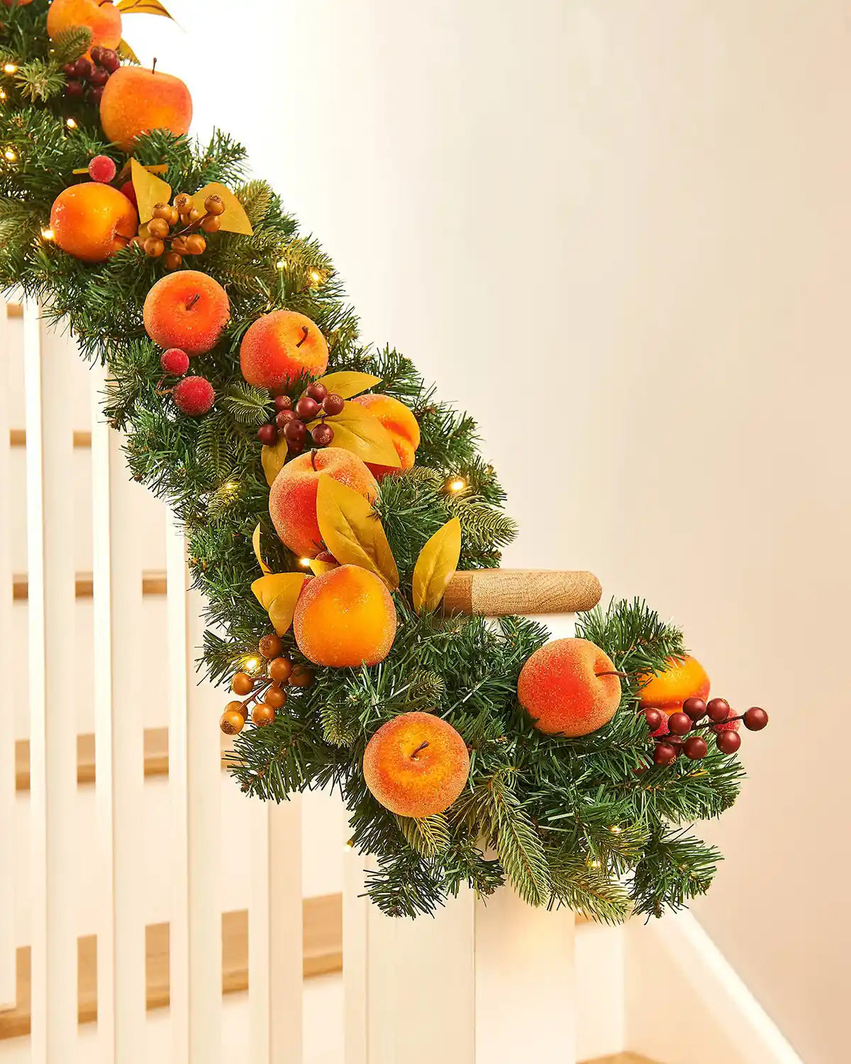 Decorative Christmas garland and  oranges and peaches on a staircase banister against a Cream background