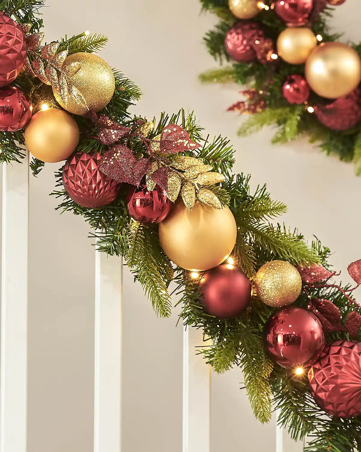 Decorative Christmas garland with burgundy and gold ornaments on a neutral background
