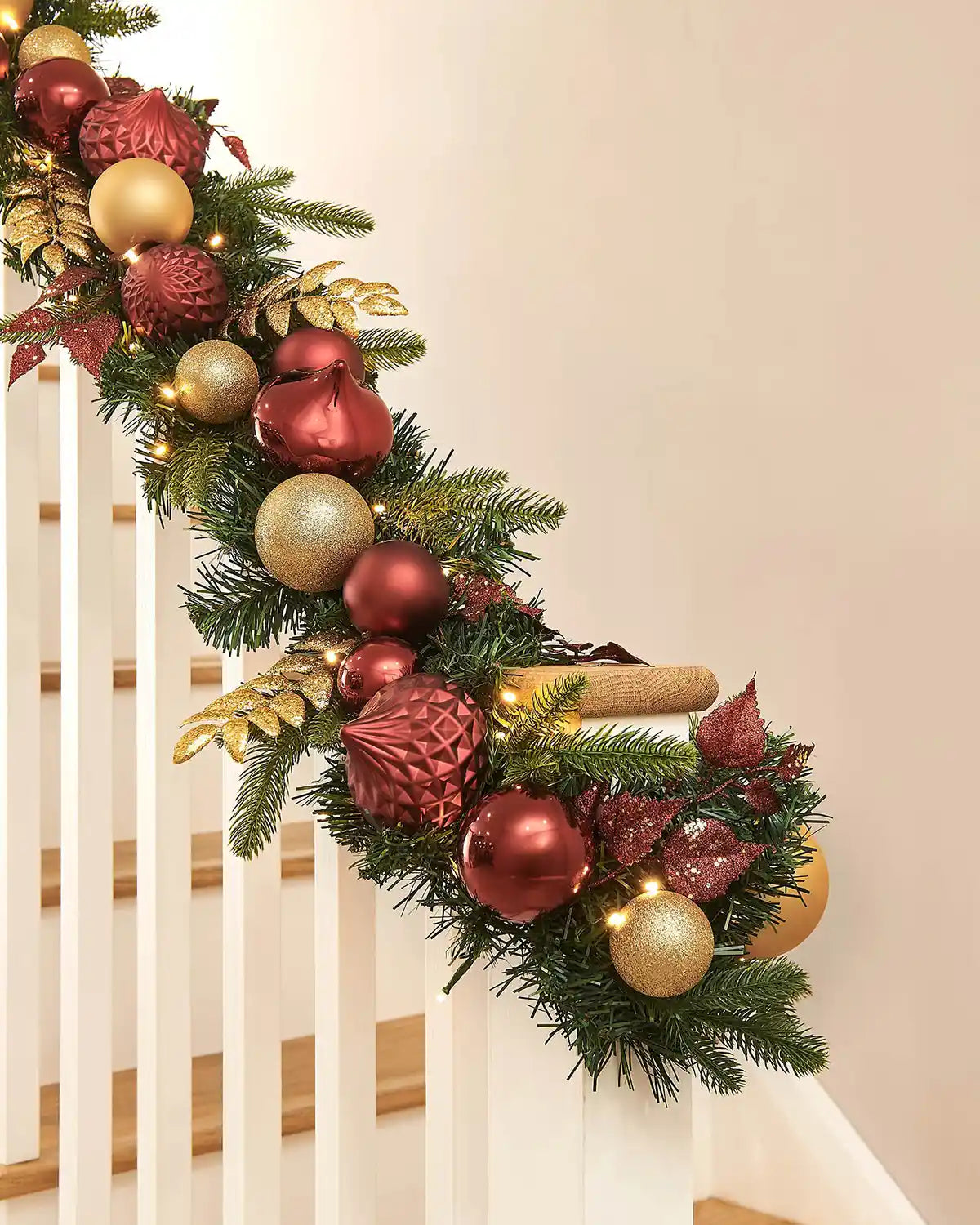 Decorative Christmas garland with burgundy and gold ornaments on a staircase banister
