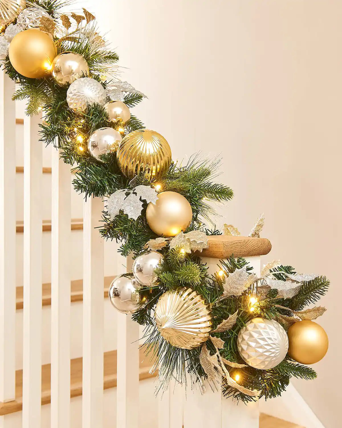 Decorative Christmas garland with gold and silver ornaments on a staircase.