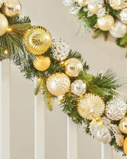 Decorative Christmas garland with gold and silver ornaments on a wooden staircase banister against a neutral background