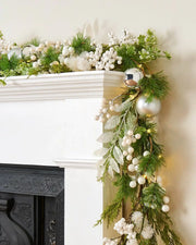 Decorative Christmas garland with greenery and white berries on a fireplace mantle.