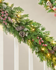 Decorative Christmas garland with lights, pine cones, and berries on a  staircase banister neutral wall.
