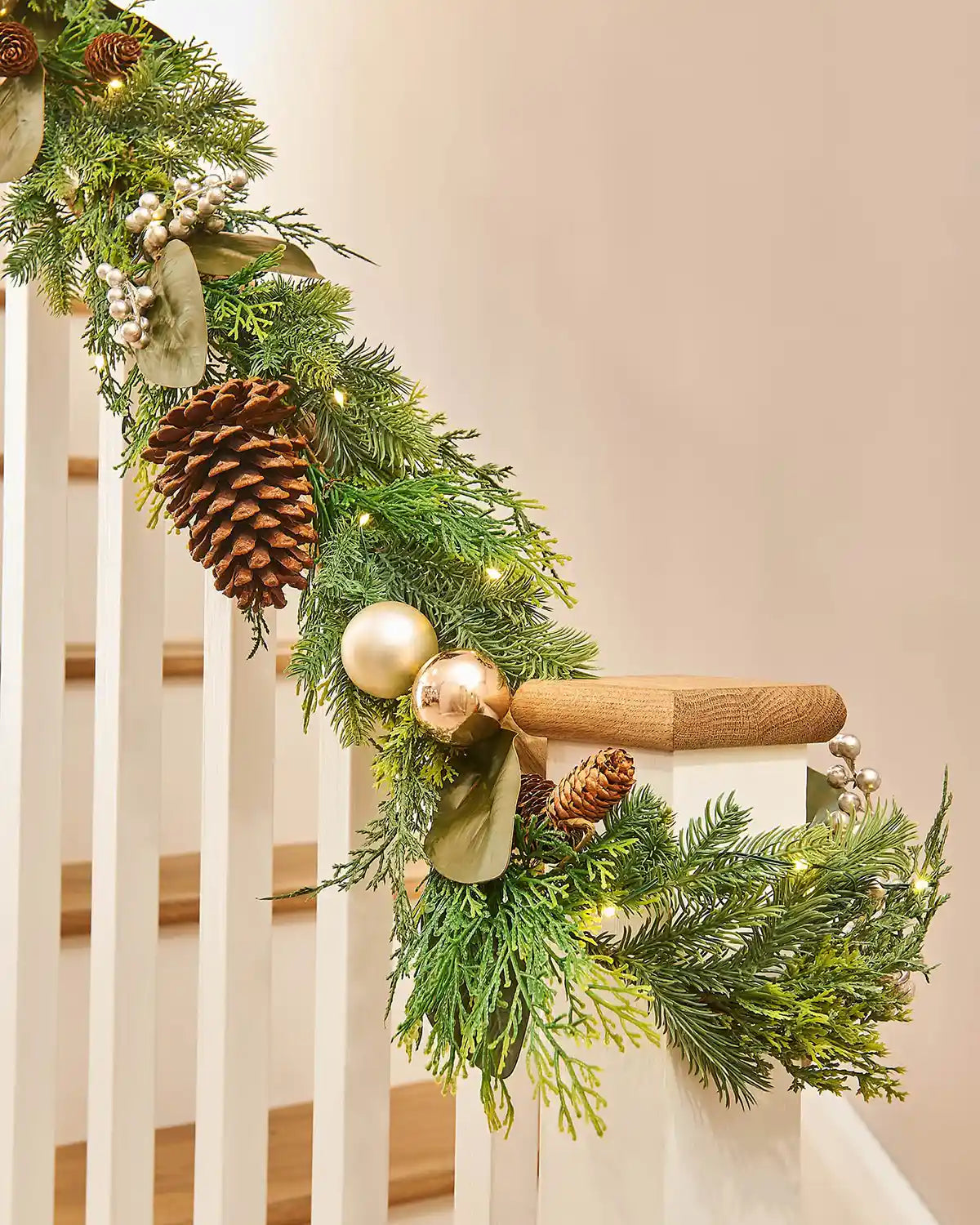Decorative Christmas garland with pine cones and ornaments on a staircase.