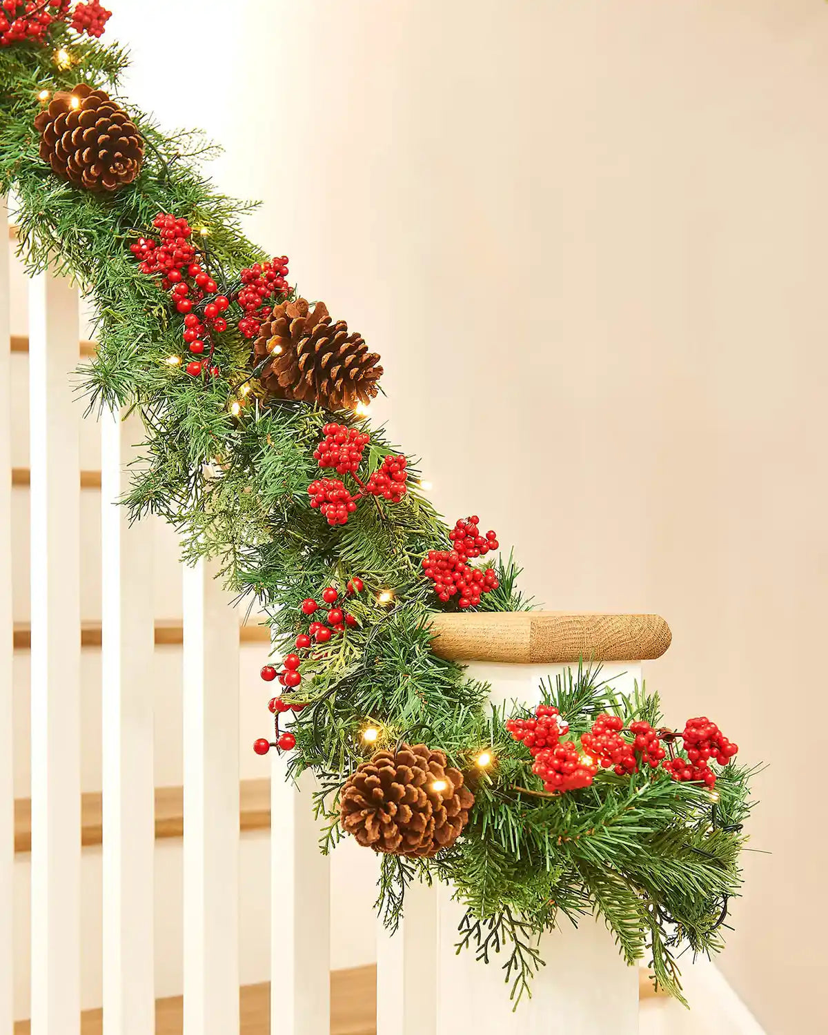 Decorative Christmas garland with pine cones and red berries on a staircase.