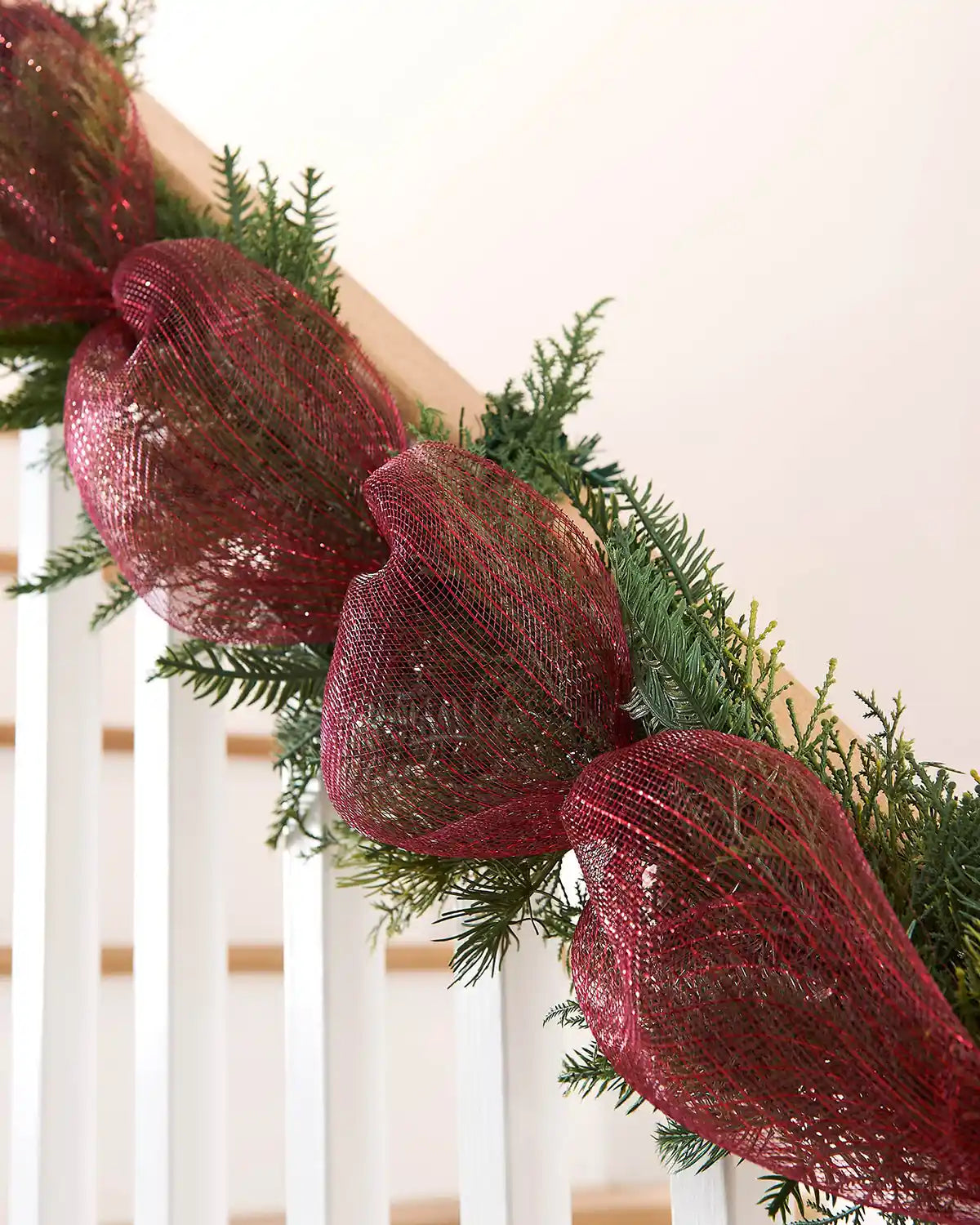 Decorative Christmas garland with red mesh ribbon and greenery on a white staircase banister