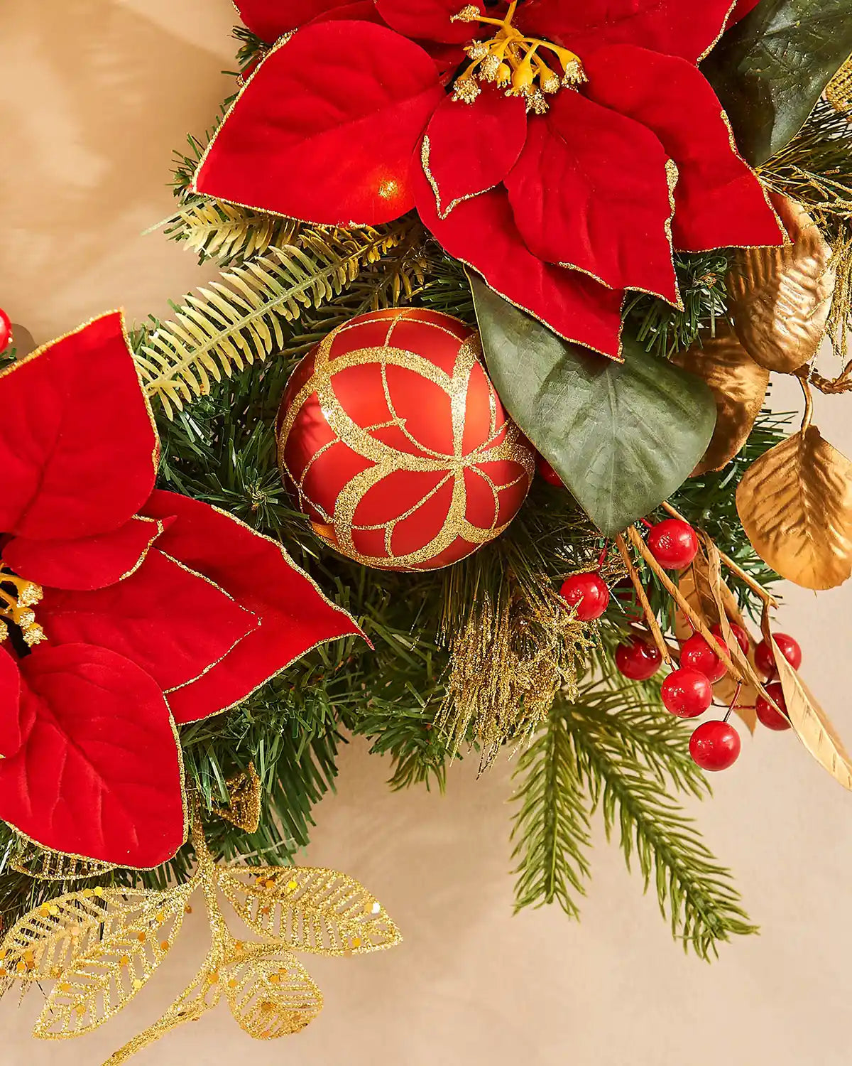 Decorative Christmas garland  with red poinsettias, gold leaves, and red berries on a beige background.