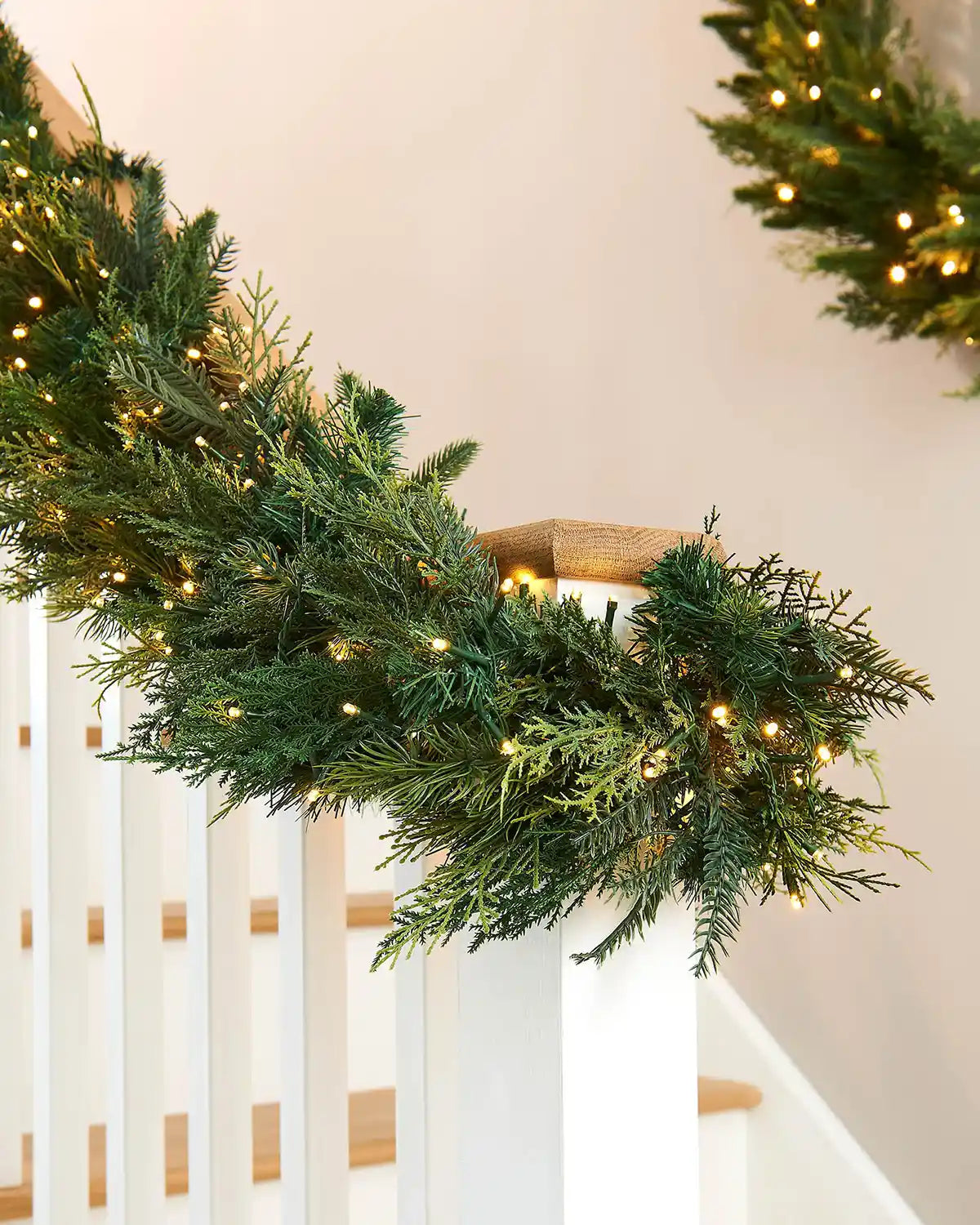 Decorative Christmas garland with warm white cluster lights on a white railing.