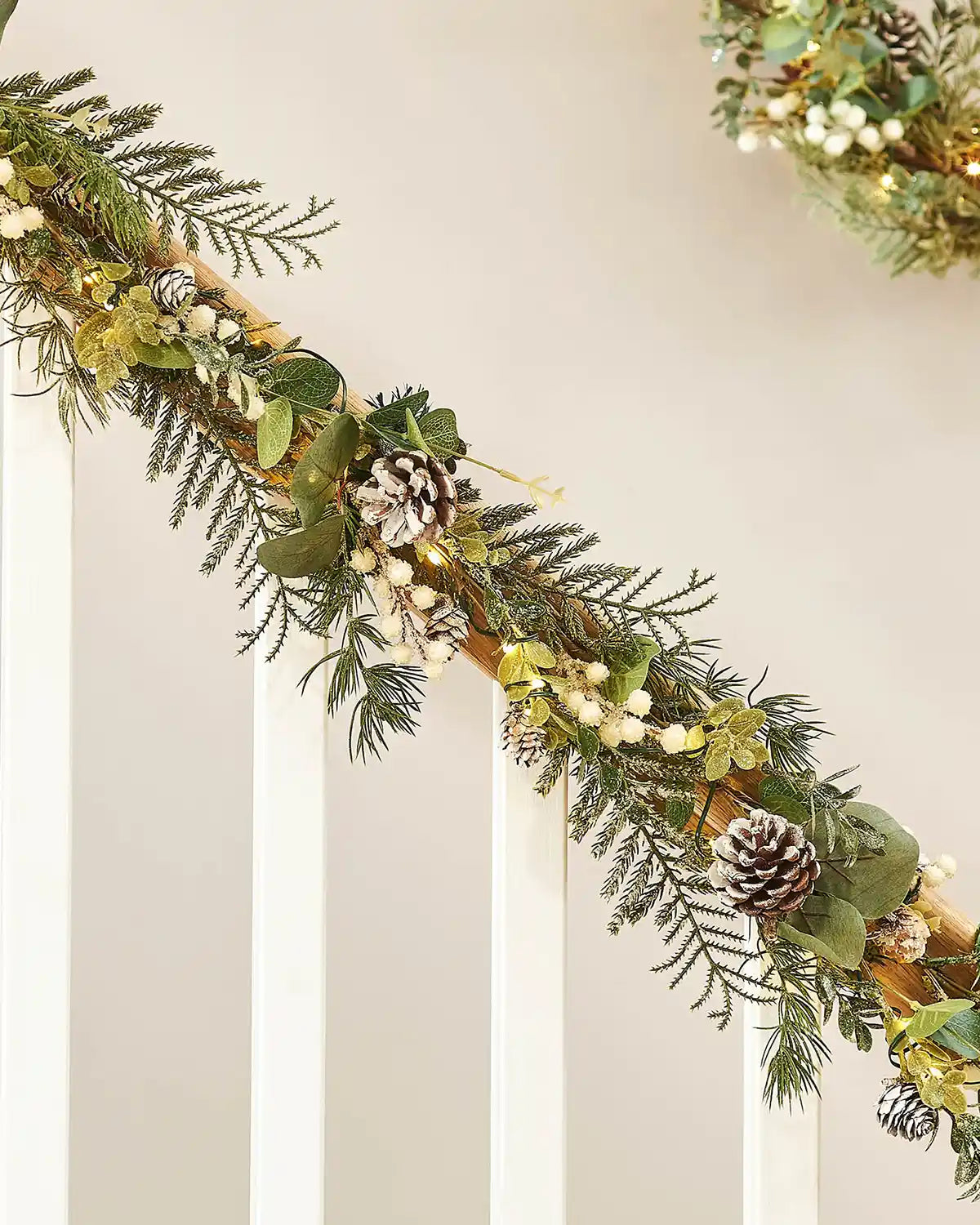 Decorative Christmas garland with white berries, lights and pinecones on a neutral background