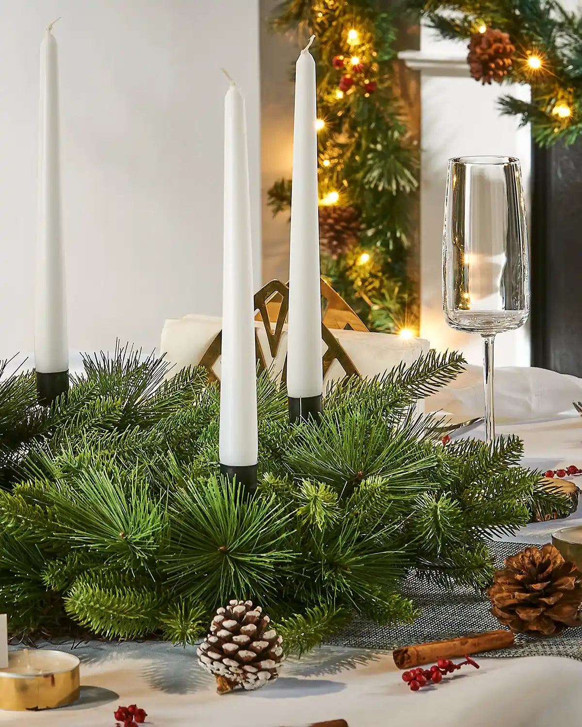 Decorative Christmas table setting with candles, greenery, and pinecones on a small green wreath