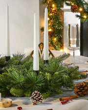 Decorative Christmas table setting with candles, greenery, and pinecones on a small green wreath