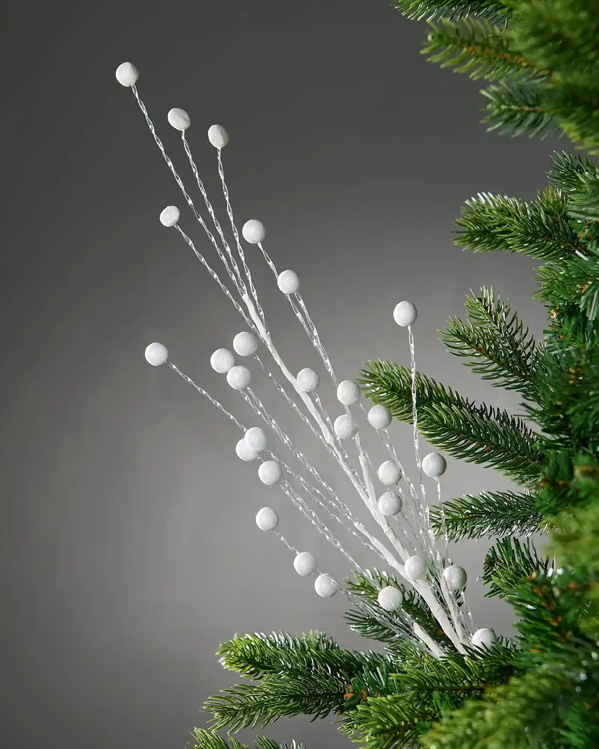 Decorative Christmas tree branch with white berries against a grey background