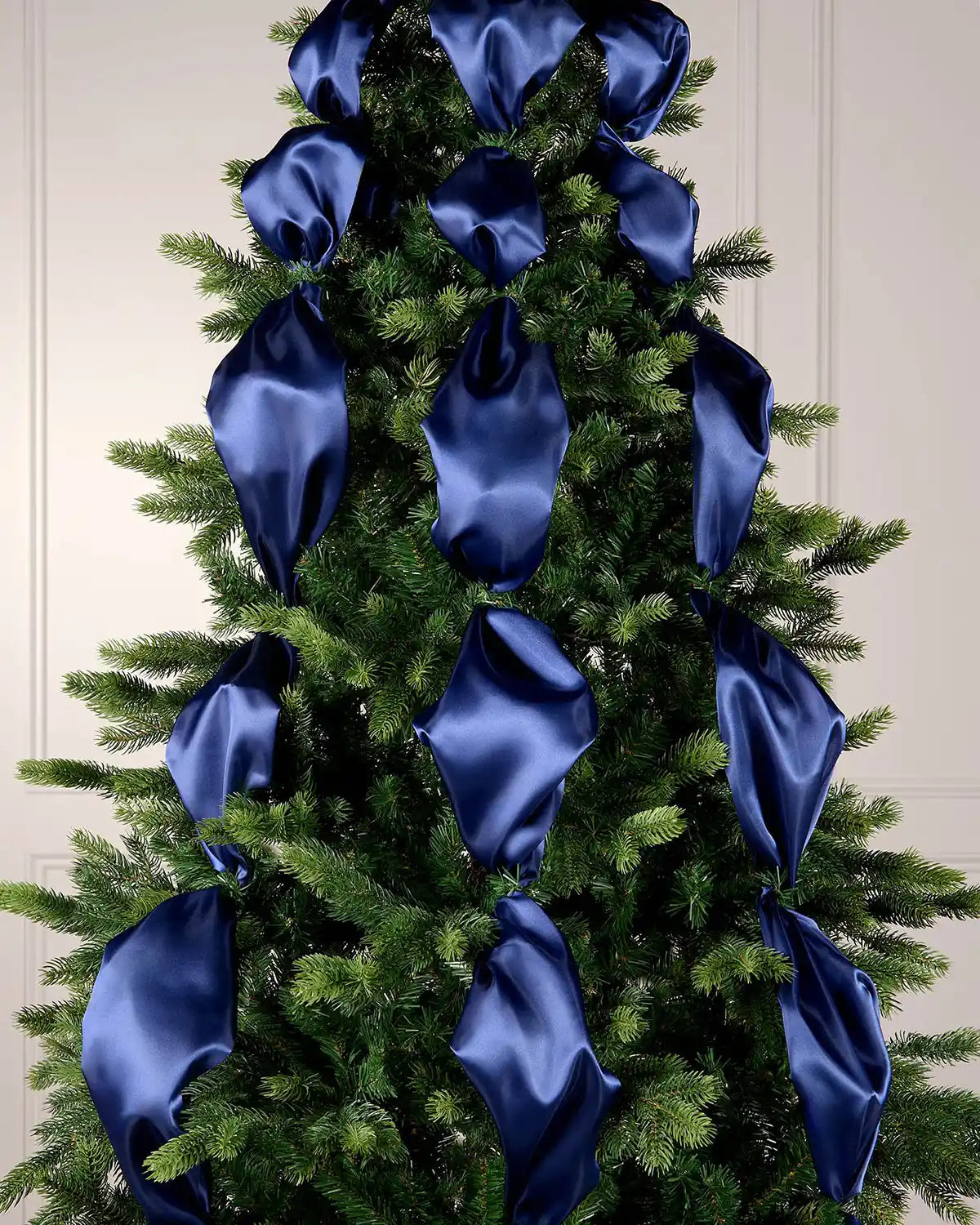Decorative Christmas tree with blue ribbons against a white wall