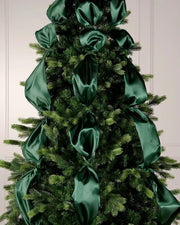 Decorative Christmas tree with large green ribbons against a white wall.