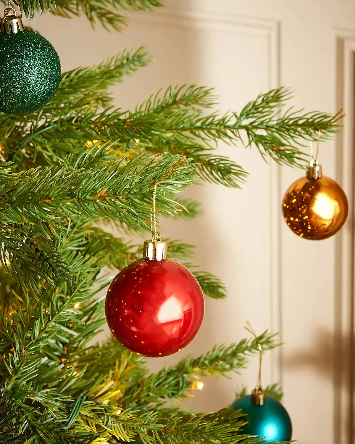 Decorative Christmas tree with red, gold, and green baubles against a cream background
