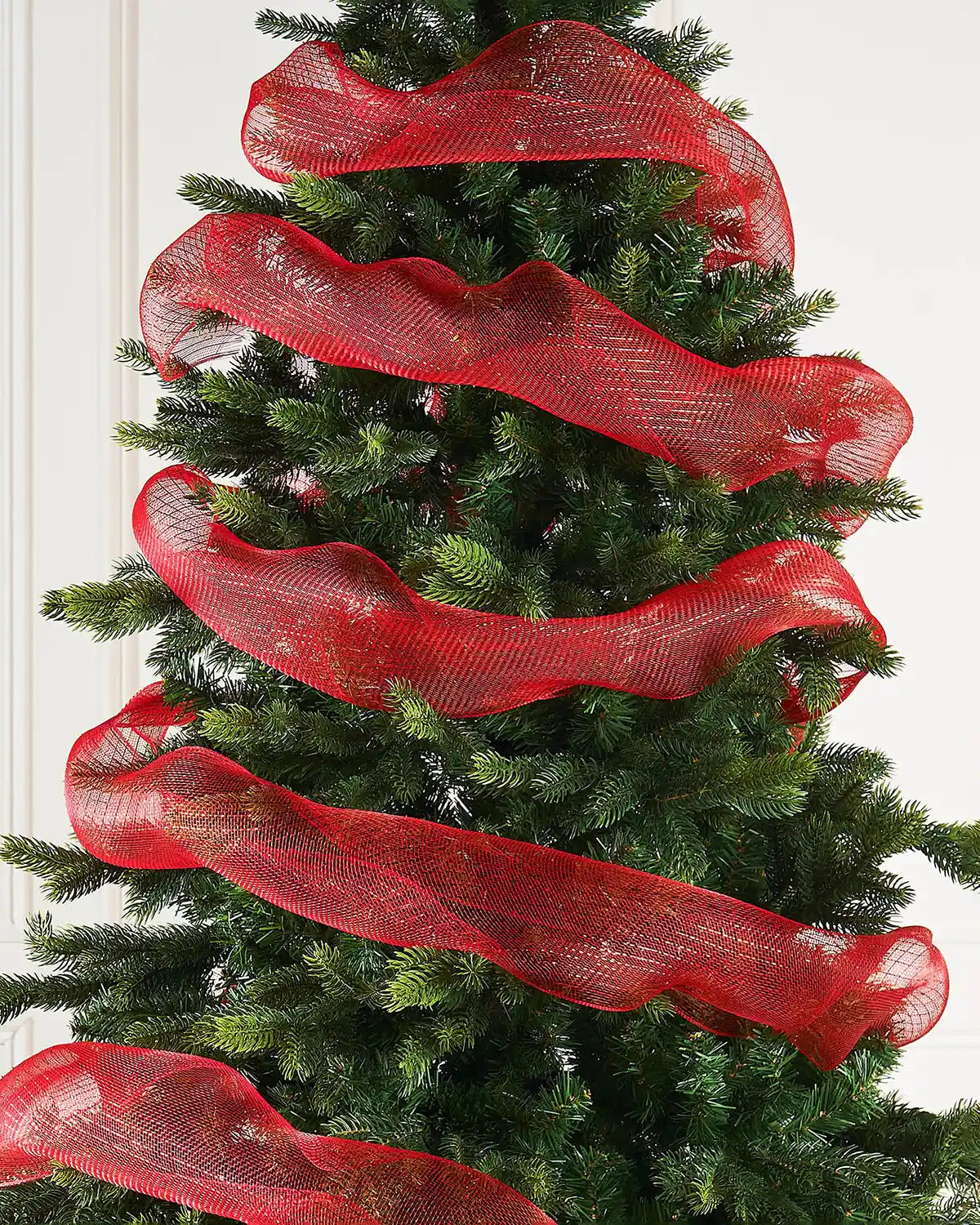 Decorative Christmas tree with red ribbons against a cream wall