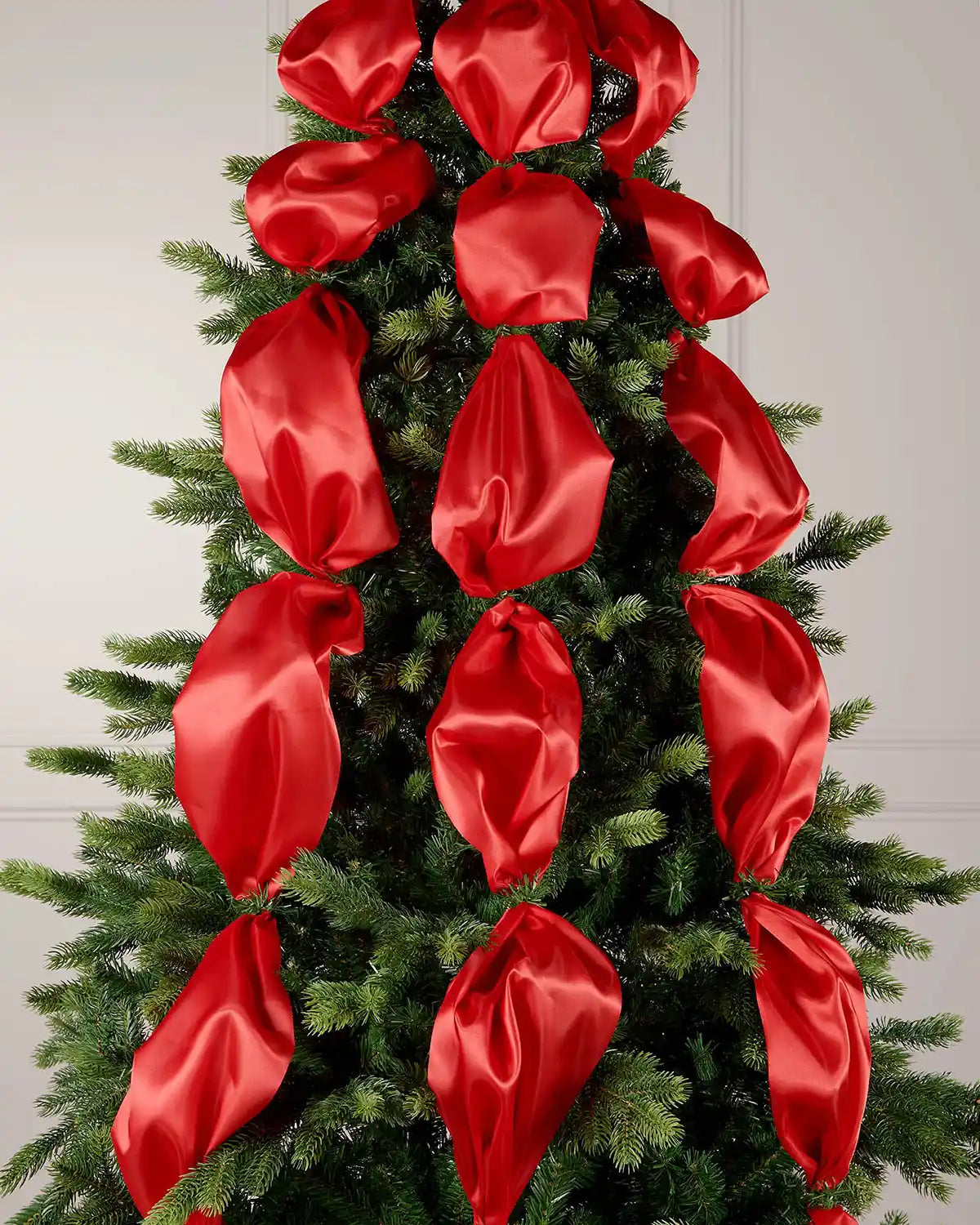 Decorative Christmas tree with red satin ribbon on a plain background