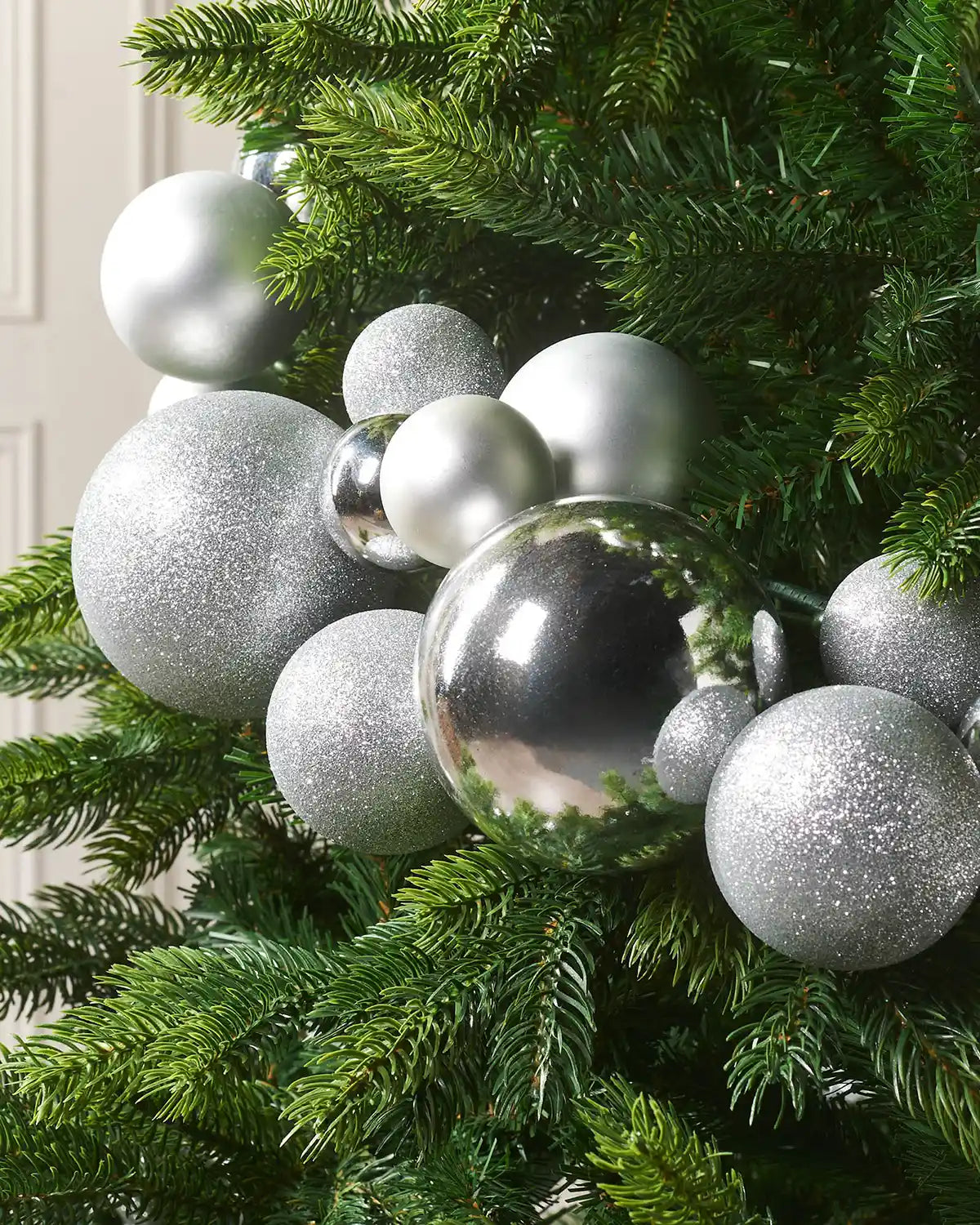 Decorative Christmas tree with silver bauble garland against a cream wall.
