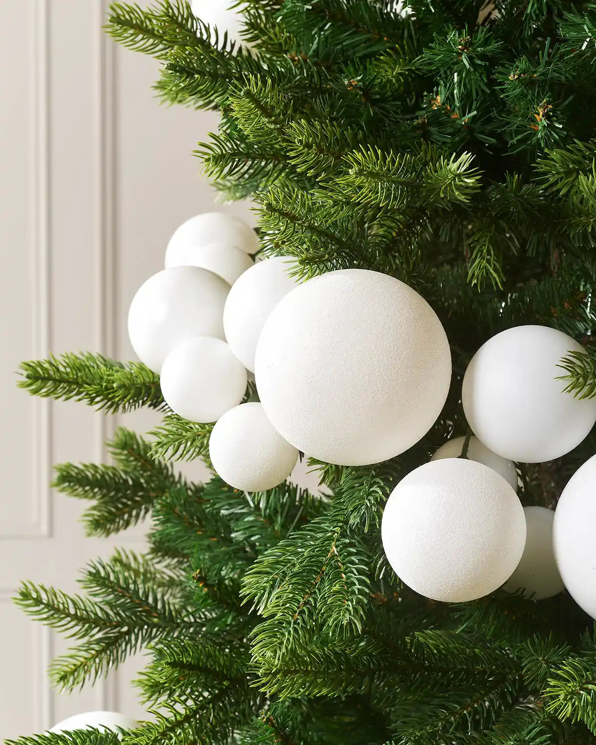 Decorative Christmas tree with white bauble garland against a cream wall.
