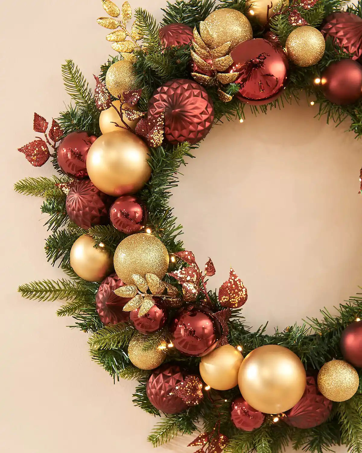 Decorative Christmas wreath with gold and red baubles on a beige background