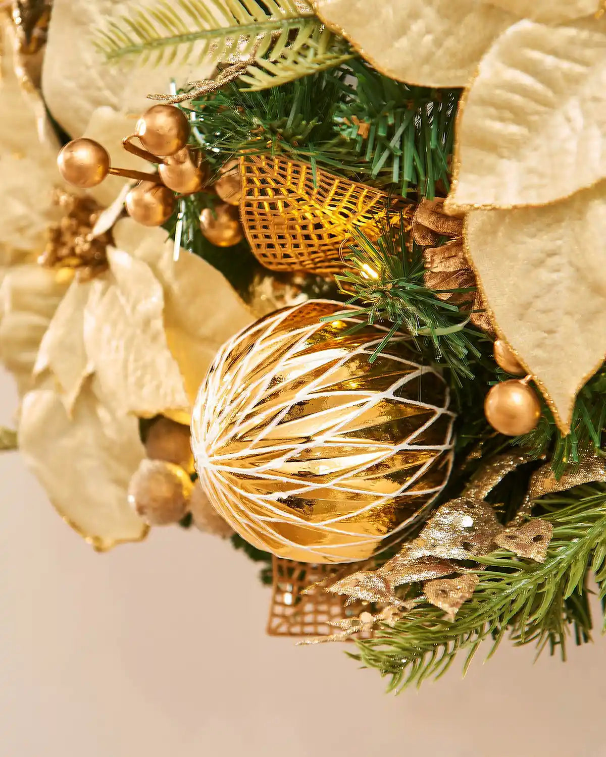 Decorative Christmas wreath with gold baubles and green leaves on a neutral background