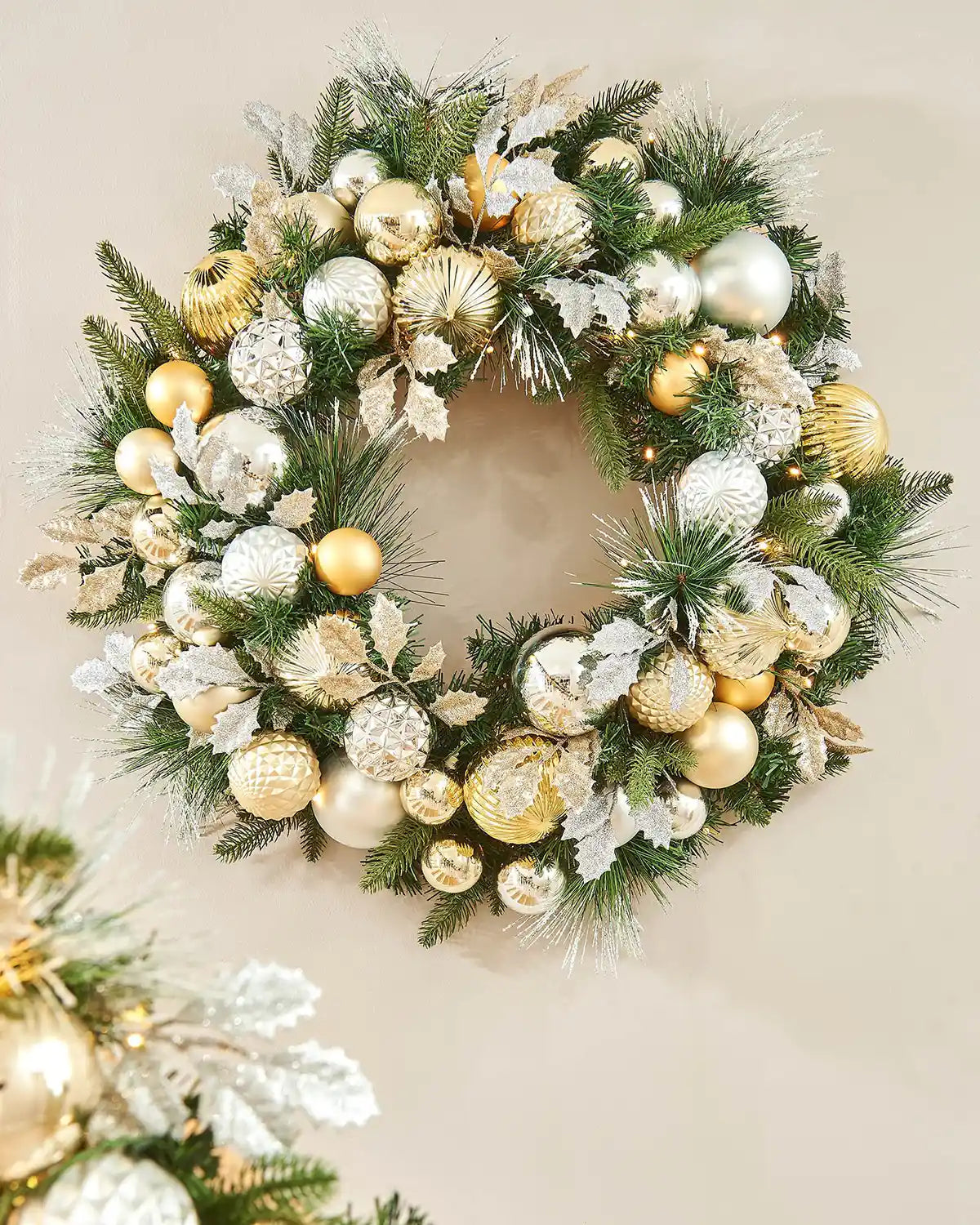 Decorative Christmas wreath with gold, silver, and white baubles on a neutral background