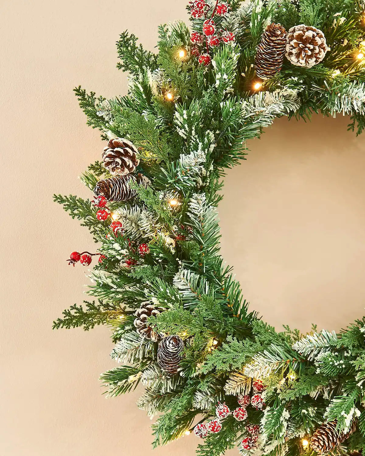 Decorative Christmas wreath with greenery, pinecones, and red berries on a beige background