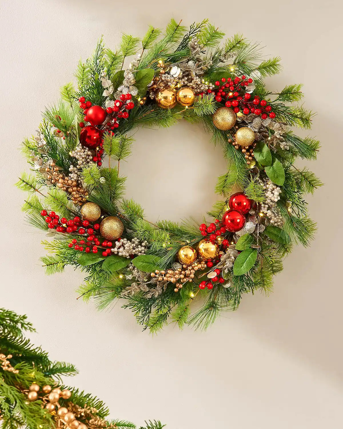 Decorative Christmas wreath with greenery, red berries, and gold ornaments on a cream background