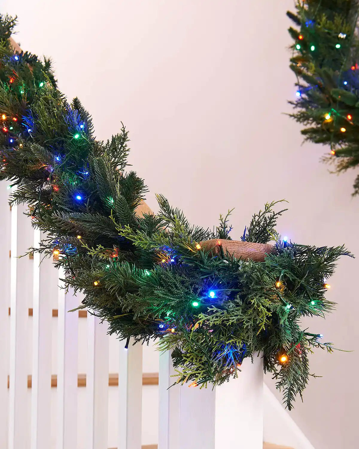 Decorative Christmas wreath with lights on a white staircase railing.