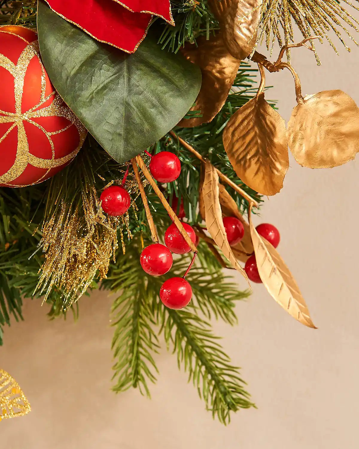 Decorative Christmas wreath with red berries, gold leaves, and a red ornament on a beige background.