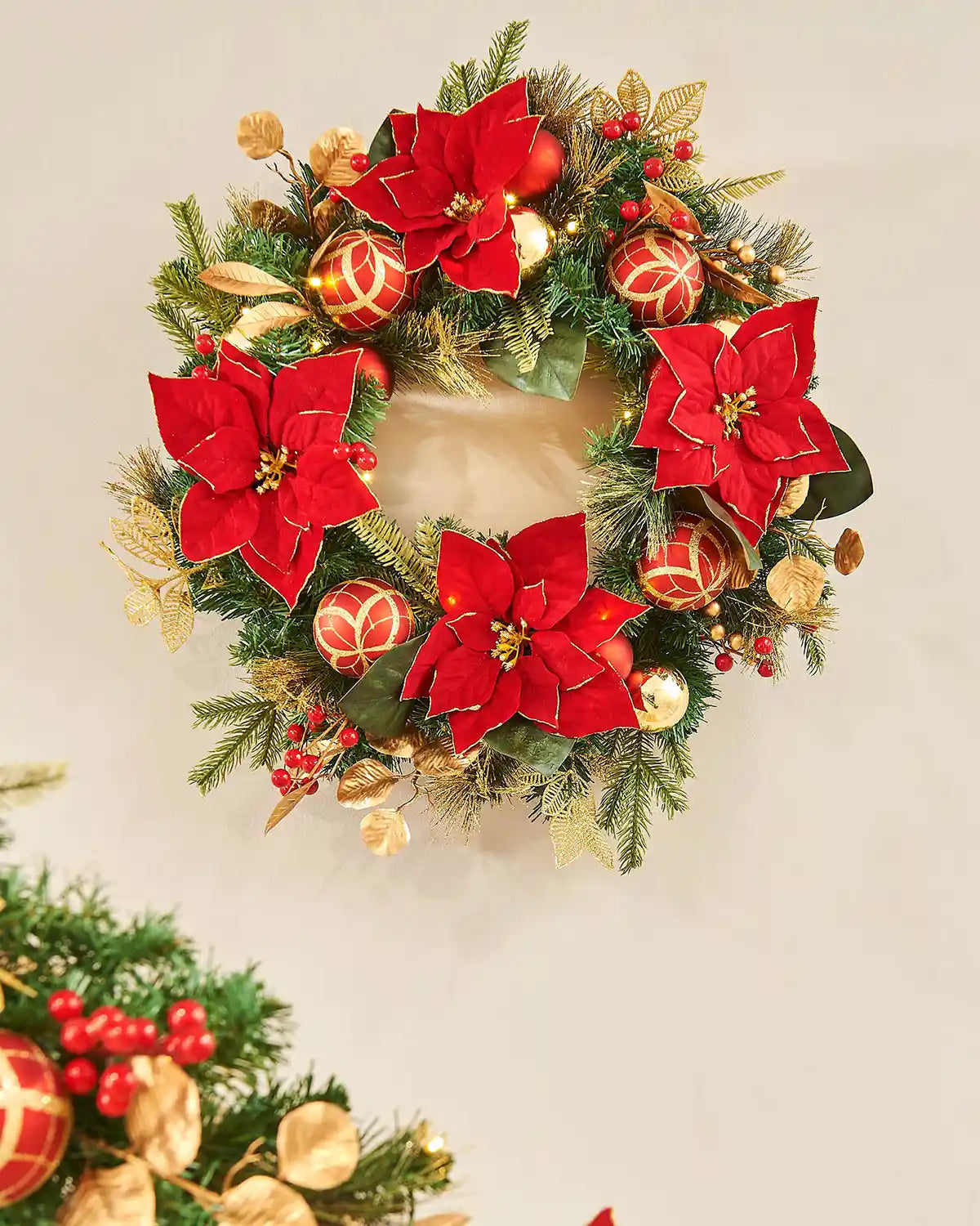 Decorative Christmas wreath with red poinsettias and gold ornaments on a cream background