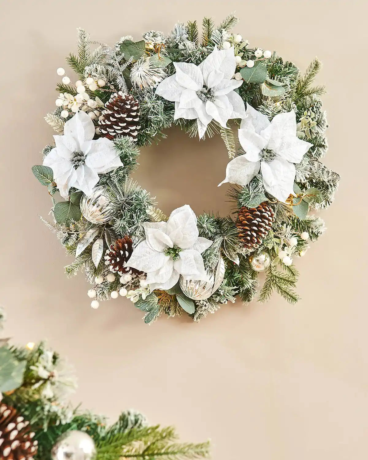 Decorative Christmas wreath with white flowers, pinecones, and greenery on a beige background