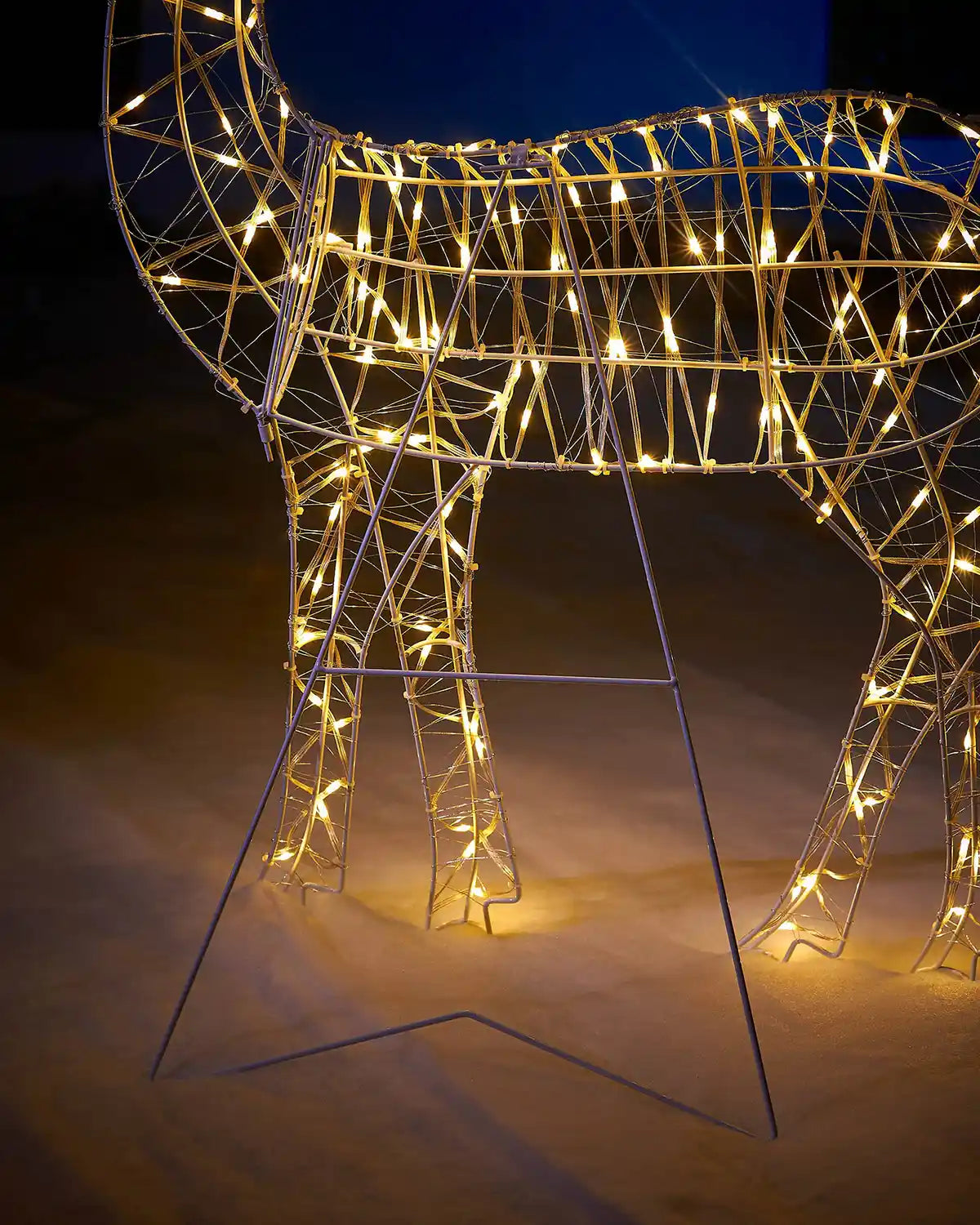 Decorative LED deer illuminated with warm lights against a snowy garden floor and a stand to support the reindeer