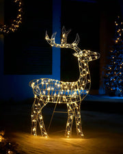 Decorative LED reindeer figure illuminated in a dark outdoor setting with Christmas lights.