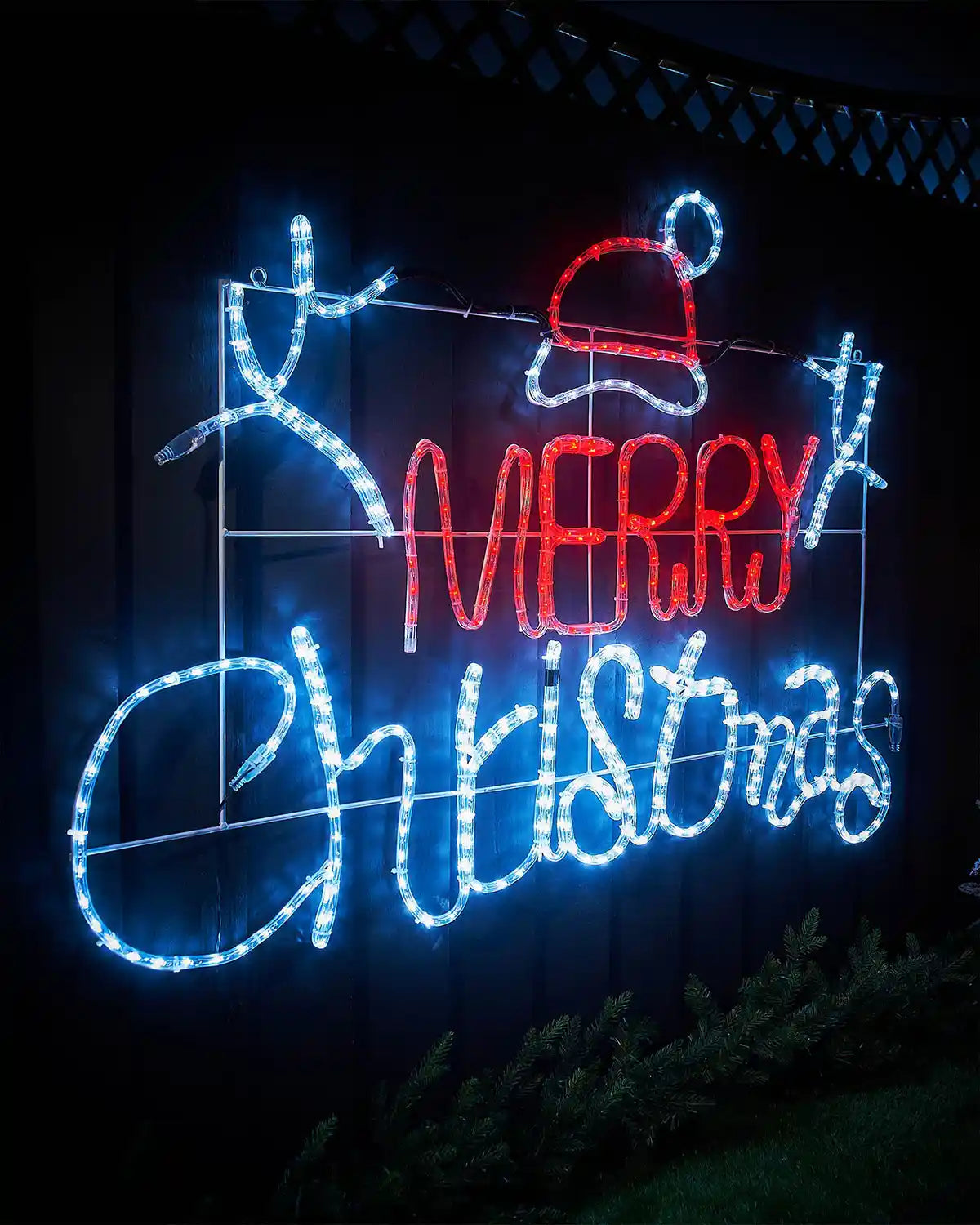 Decorative LED sign with 'Merry Christmas' text and Santa hat on a garden fence