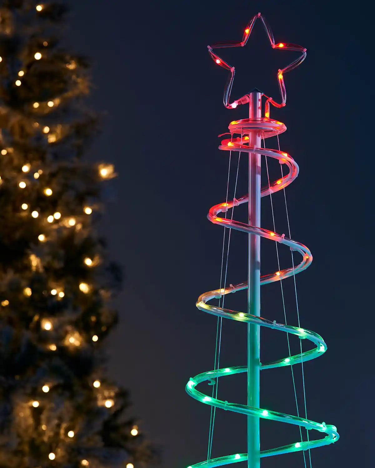 Decorative LED spiral tree with star top against a dark background with other decorated tree