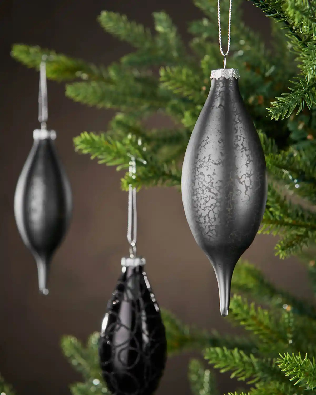 Decorative black baubles hanging on a Christmas tree with a brown blurry background