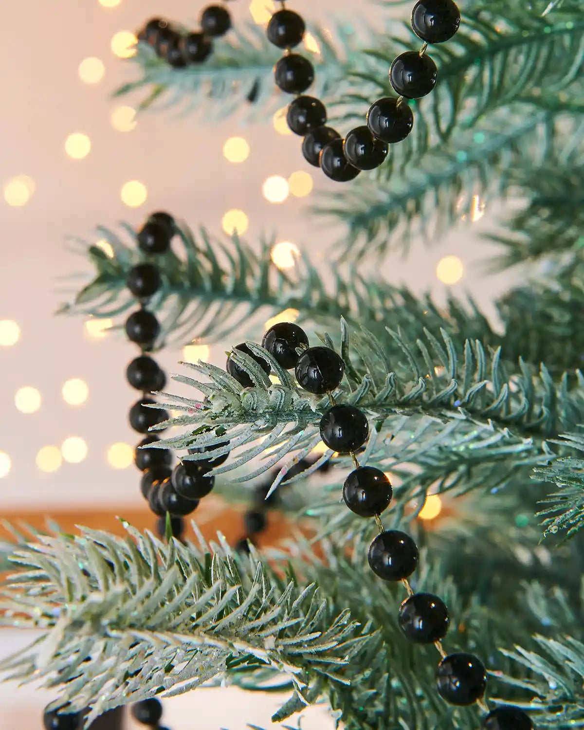 Decorative black bead garland on a branch with a soft, blurred light background