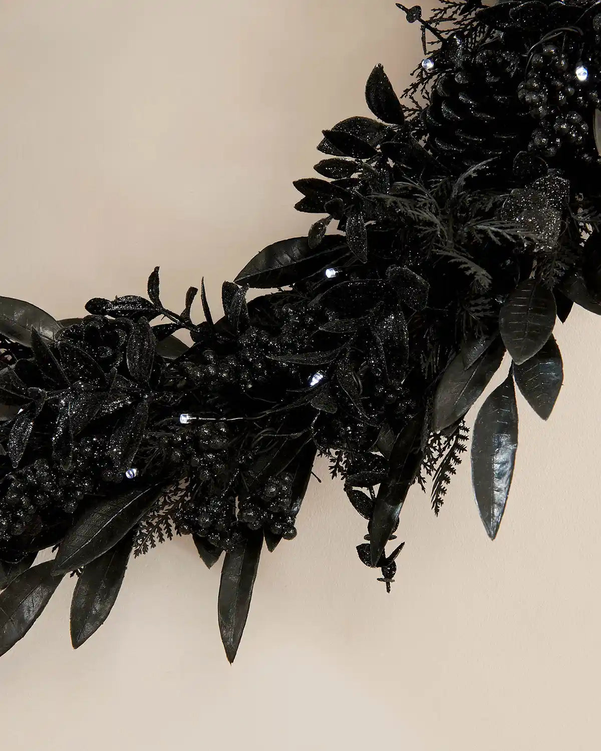 Decorative black wreath with leaves and small ice white lights on a beige background
