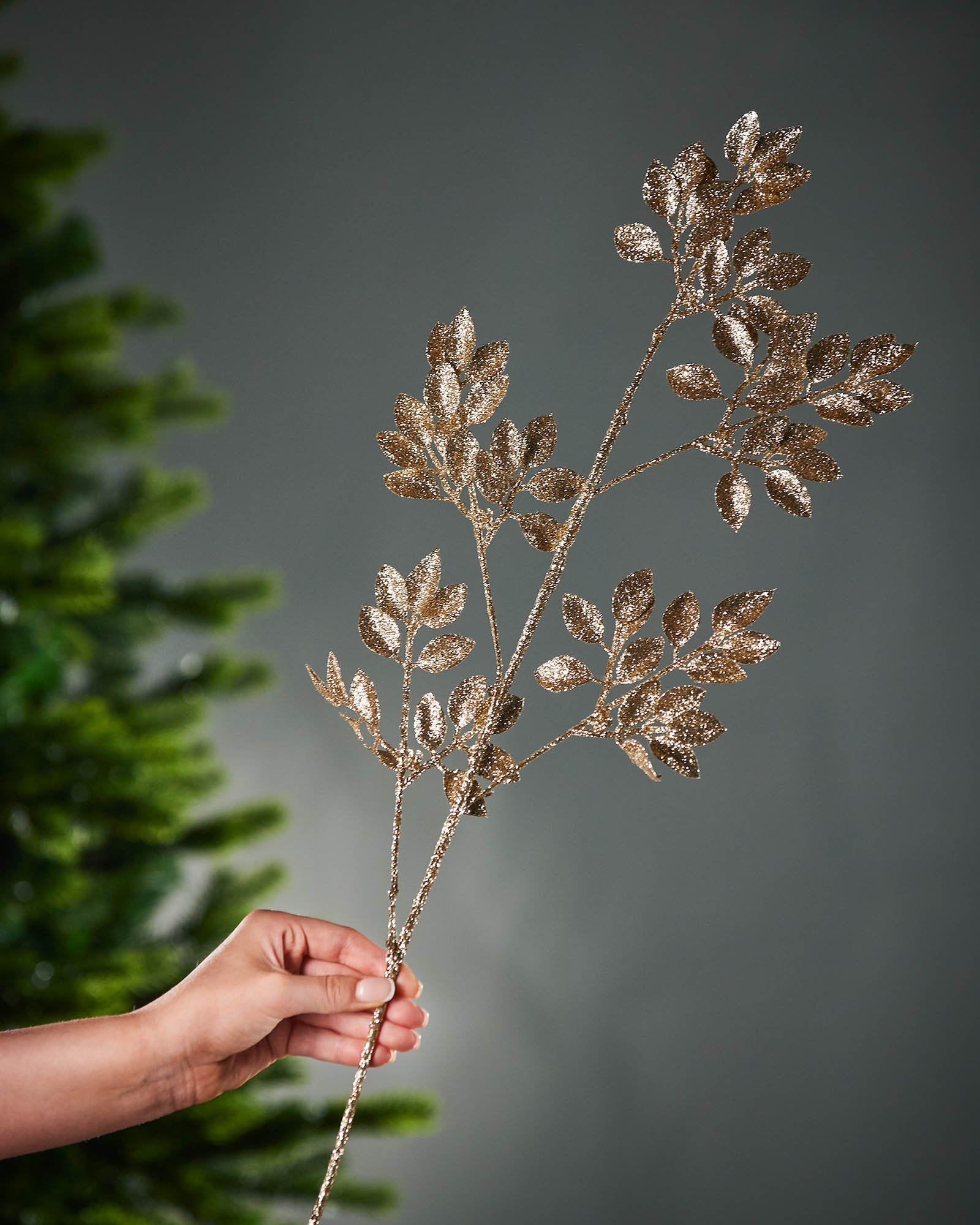 Decorative branch with glitter gold leaves held by a hand against a grey background