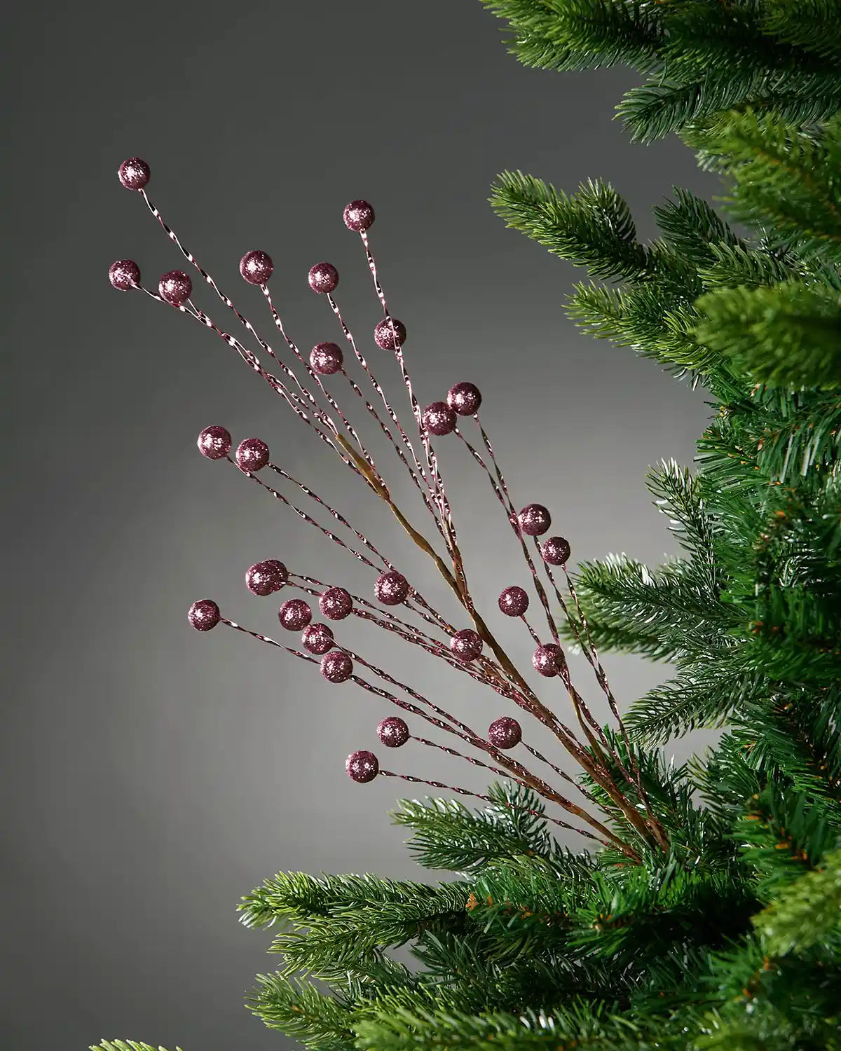 Decorative branch with pink berries on a Christmas tree against a grey background