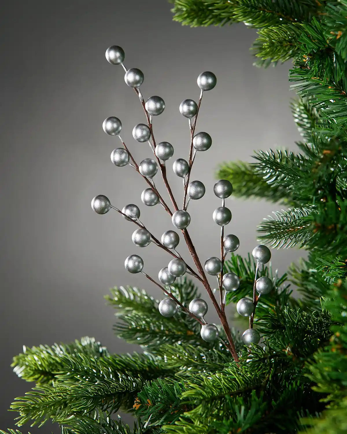 Close up of Decorative branch with silver berries on a Christmas tree against a grey background