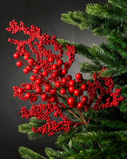 Decorative branch with small red berries and larger red berries on a Christmas tree against a grey background 