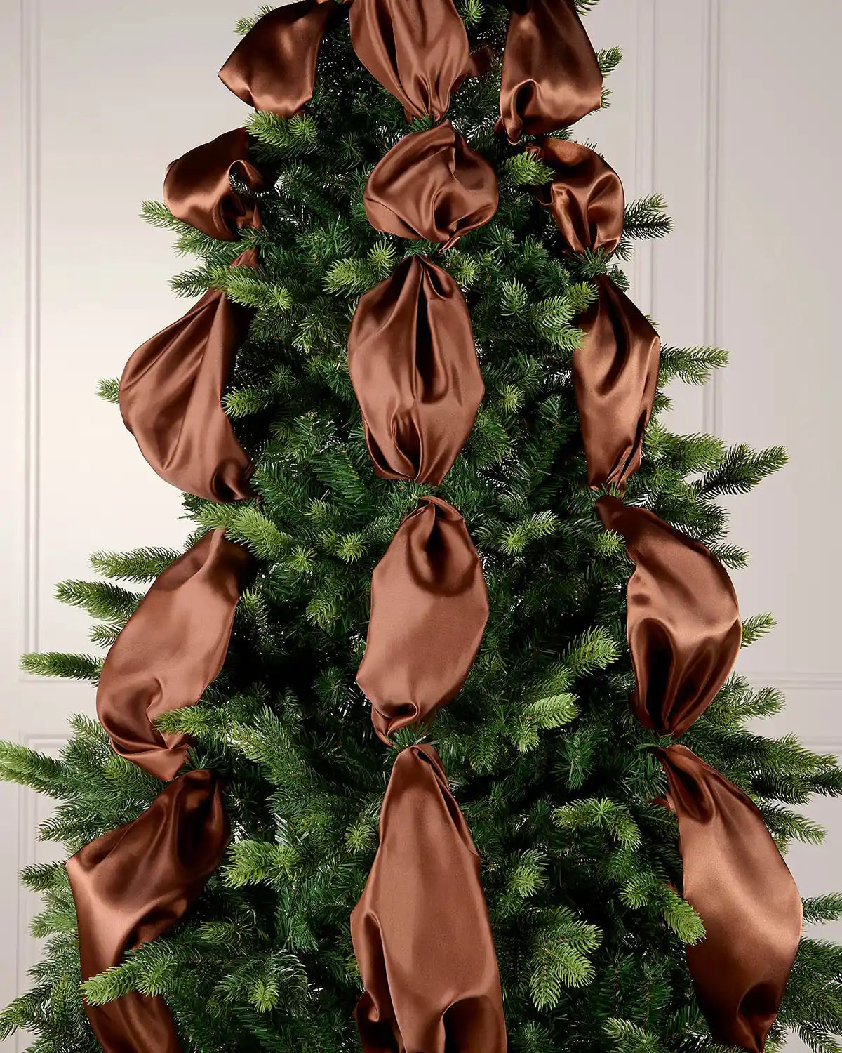 Decorative espresso ribbons on a Christmas tree against a white wall.